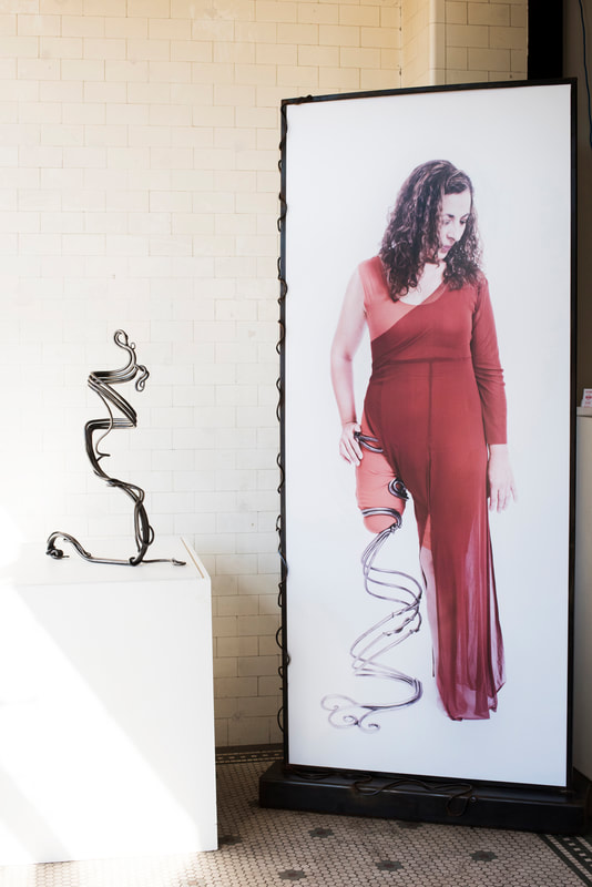 On the left is a swirled metal prosthetic leg and on the right a large photo of a white woman in a red dress wearing that leg.