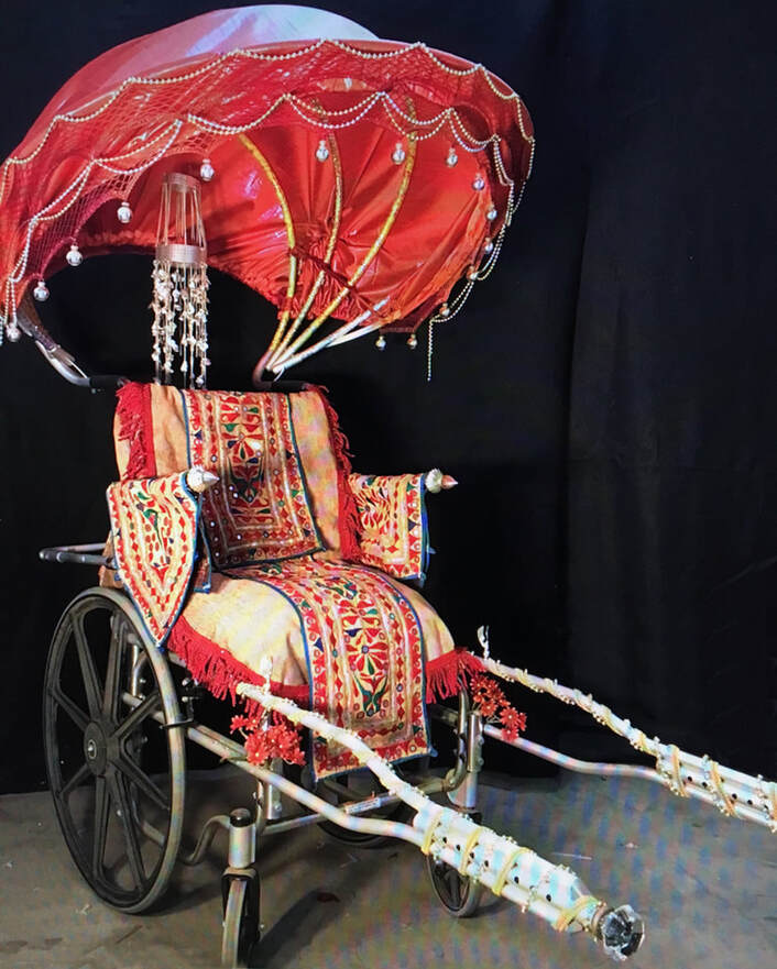 Wheelchair with bamboo and red fabric hood, tapestry seat and armrests, and trim wrapped crutch handles.
