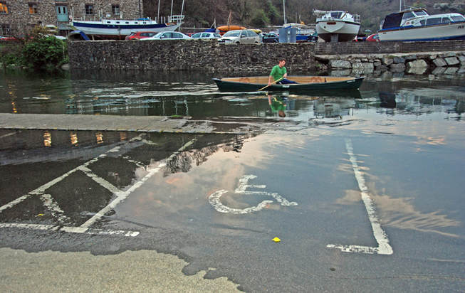 A photograph of a flloded handicapped parking space. In the background is a man rowing a boat.