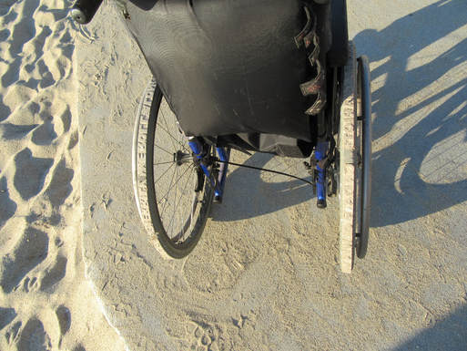 A pair of wheelchair wheels carved so that they leave imprints of words in the sand.
