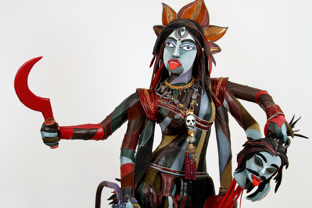 Front detail of a walker with a multi-limbed, multi-colored goddess with three eyes built in the center. She carries a red scythe in the top right hand and a severed blue demon head in the left.