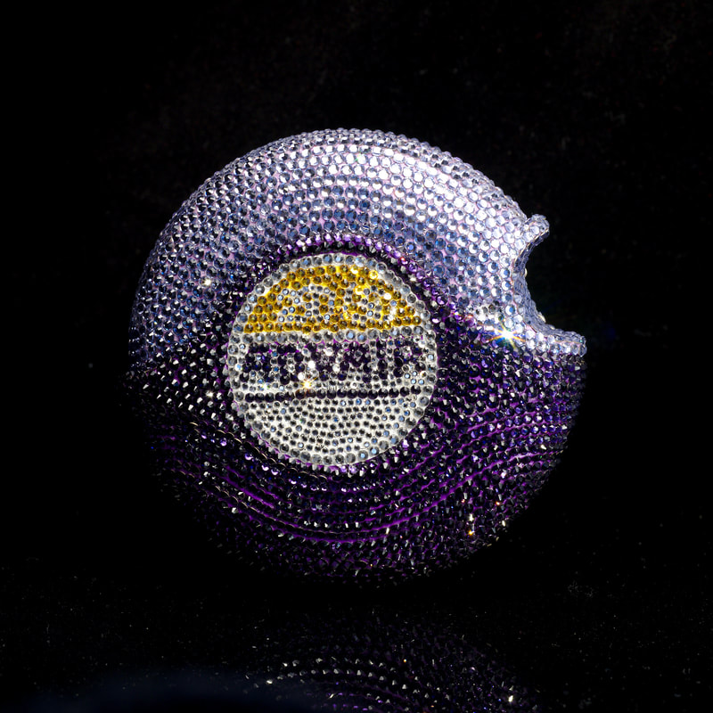 An inhaler disc covered in purple, lilac, clear, and gold rhinestones. The label reads ADVAIR.