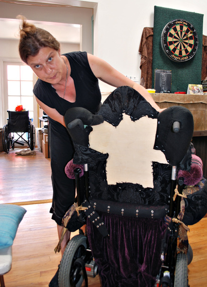 The artist with a curved needle in her mouth rebuilds the back of Driven, a wheelchair made up as an Edwardian throne.