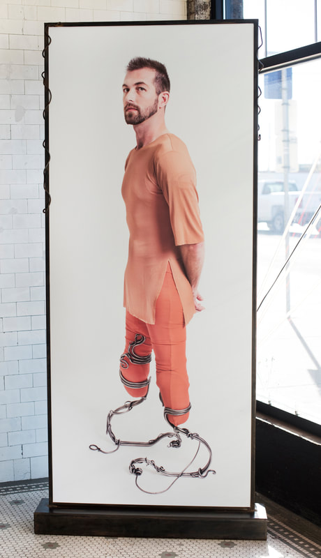 A large photo of a bearded white man in orange wearing two swirled metal prosthetic legs.
