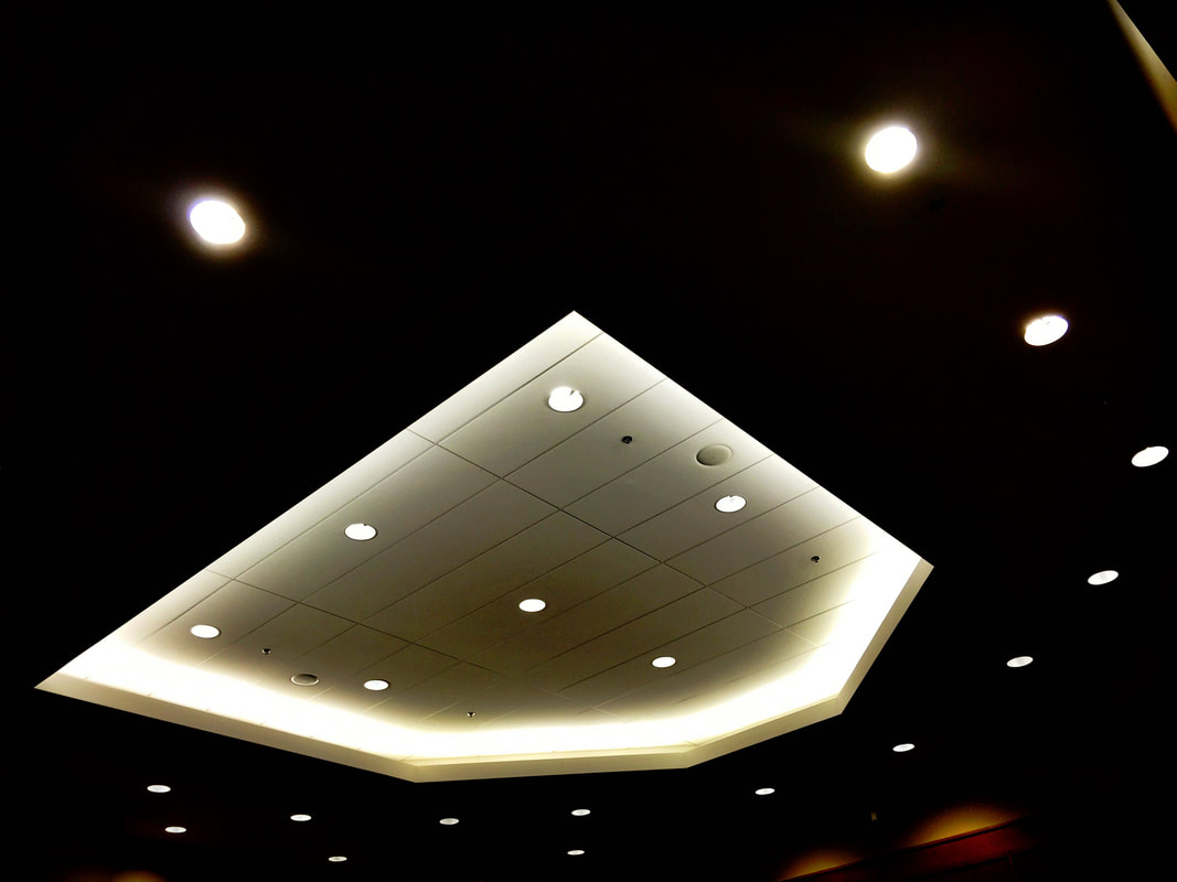 Photo of an irregular geometric ceiling with glowing lights and white paneling against a dark background with periodic rounds of white light.