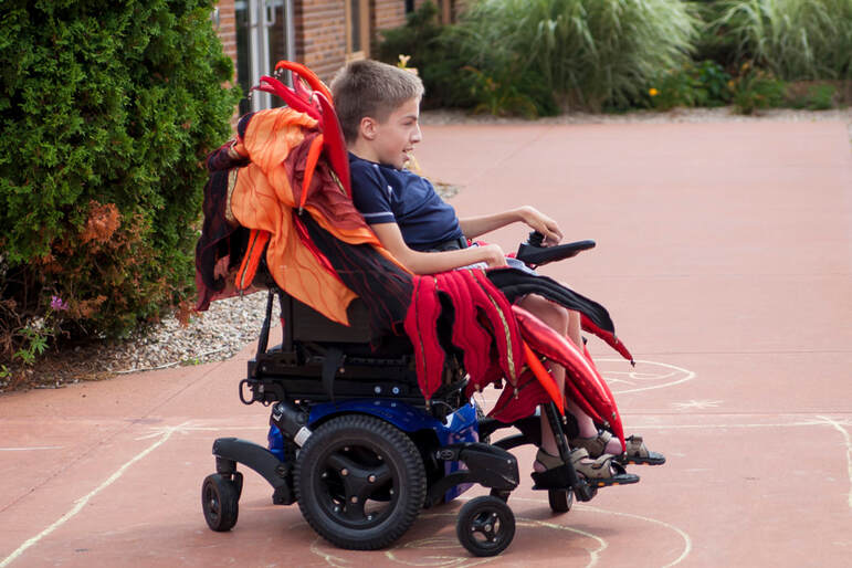 An electric wheelchair and driver with a fancy red and orange wheelchair seat cover.