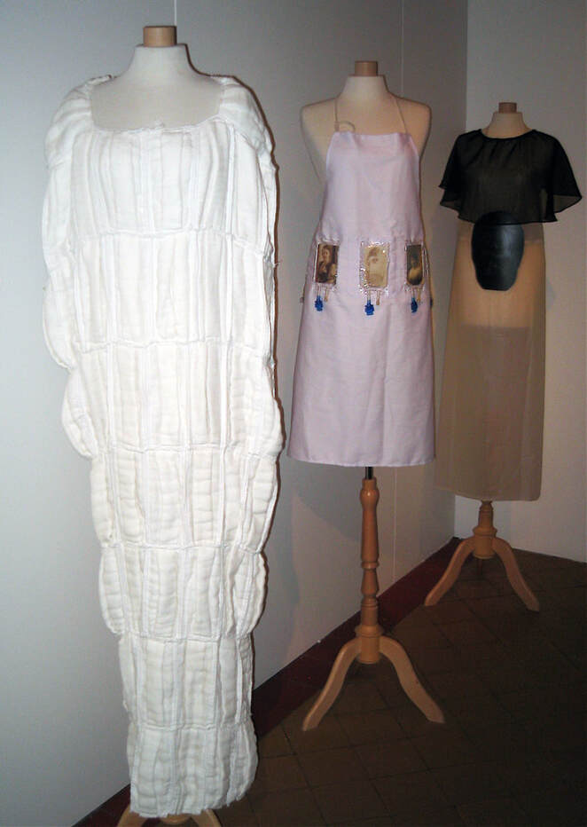 On the left are white cotton dust masks sewn into a straitjacket. In the center is a pink nurse apron with IV pouches and vintage photographs, and on the right is a beige apron with a black sheer collar and a skull x-ray.