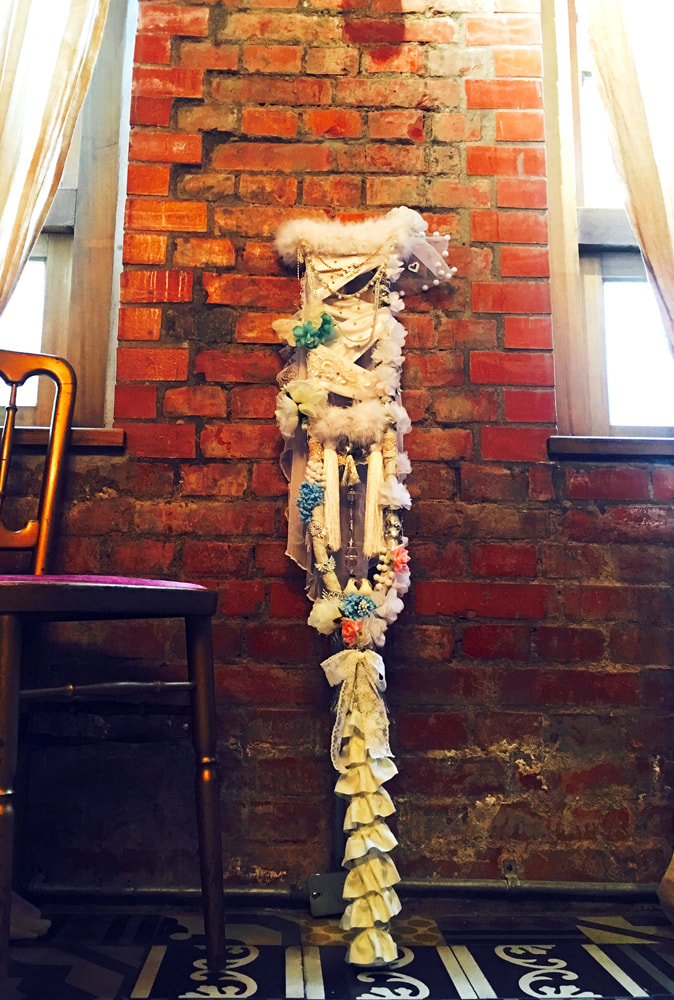 A full-sized picture of a crutch decorated with fake flowers, fruit, jewels, feathers, and ruffles.
