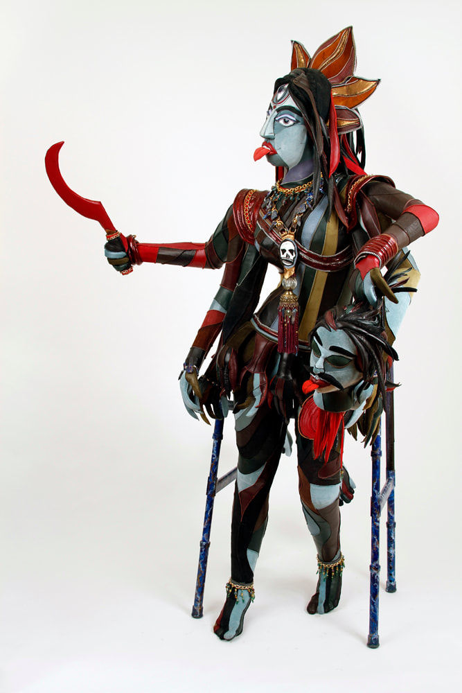 A walker with a multi-limbed, multi-colored goddess with three eyes built in the center. She carries a red scythe in the top right hand and a severed blue demon head in the left.