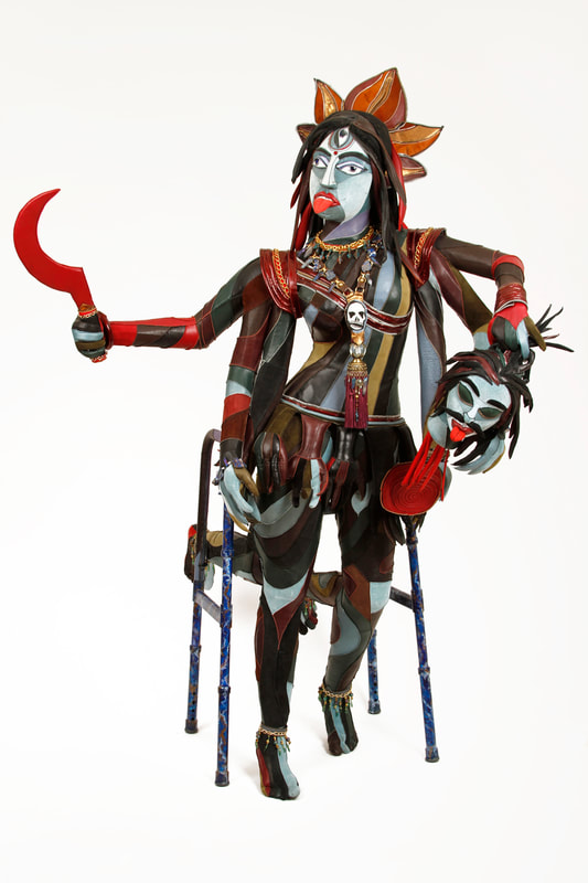 A multi-colored, multi-limbed goddess built into a walker. She has three eyes and holds a red scythe in the right upper hand and a severed demon head in the left.