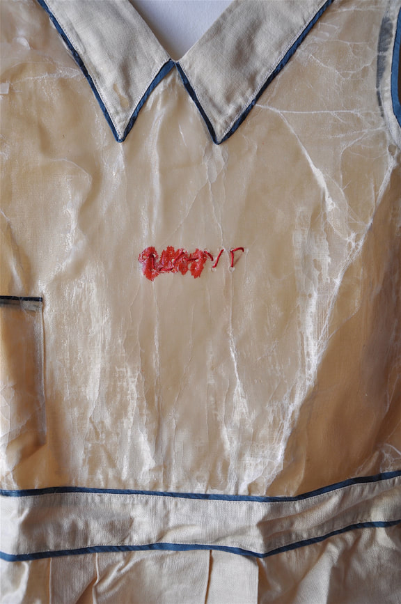 Detail of red embroidery on a waxed apron spelling out 