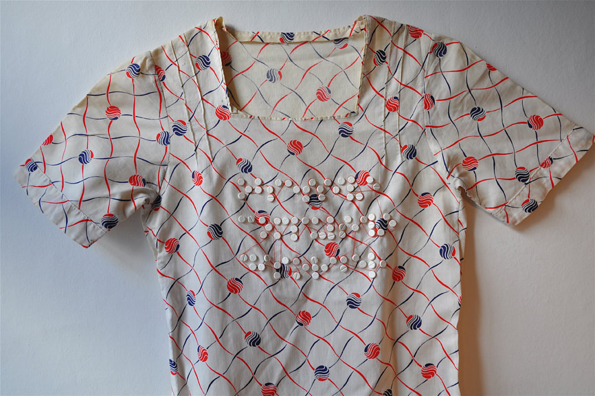 The top part of a white dress with red and blue patterns and the Braille characters for 