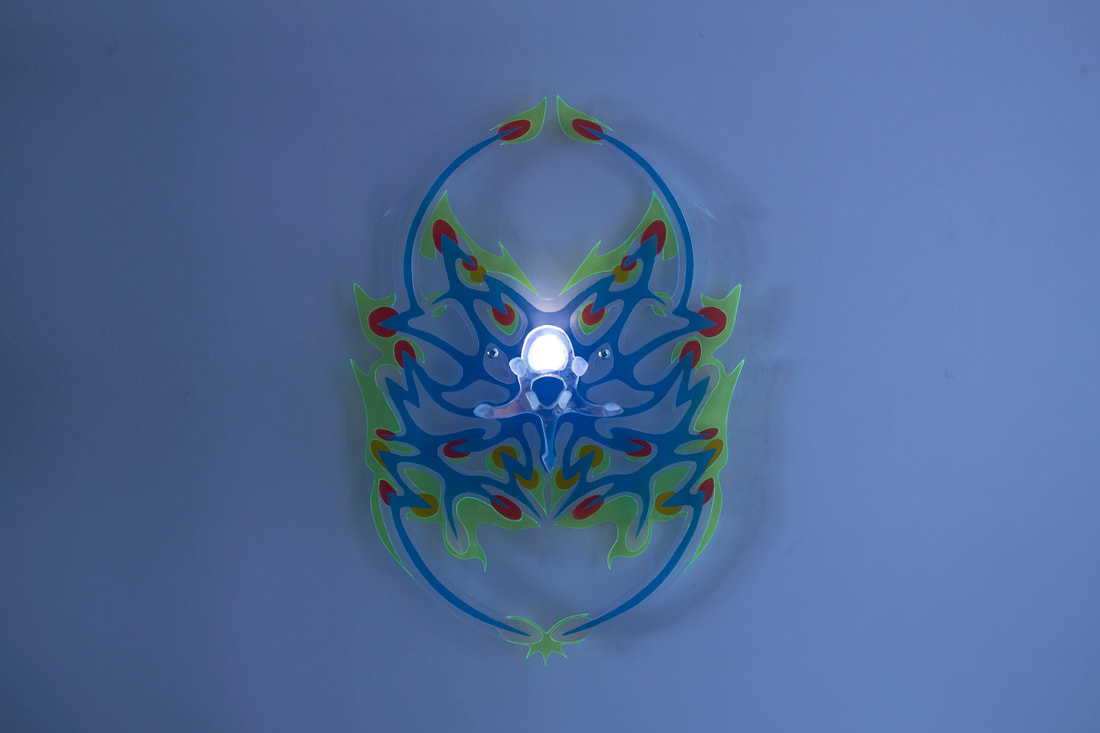 Blue, green, and red acrylic shield with a light in the center is mounted on a blue wall