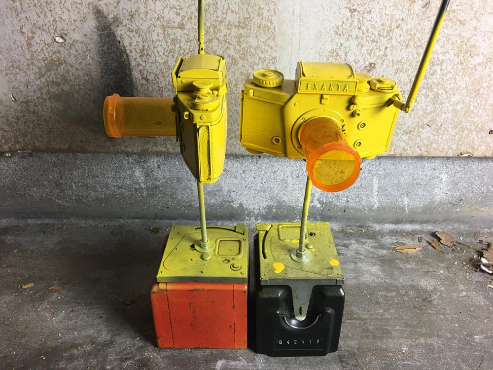 A pair of yellow painted cameras with radio antennae and prescription bottle 