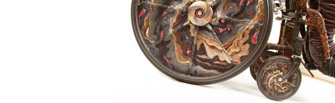 Close up of black and copper wheelchair wheels with swirls of gold, silver, and copper and accents in red and blue