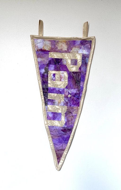 A purple and cream triangular quilted pennant with the word 