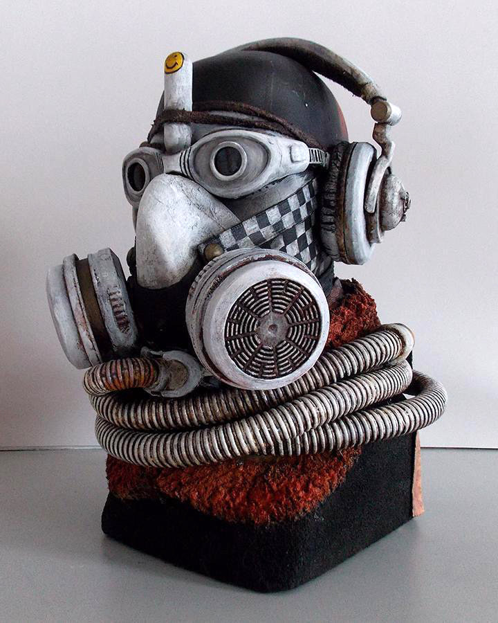 A scul-pture of a head with goggles, a respirator, a helmet, and tubing coiled araound the neck.